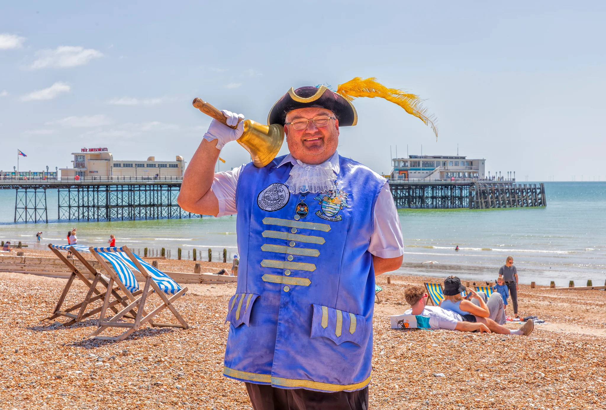 Bob Smytherman on Worthing beach with his bell over his shoulder, Worthing Pier and the English Channel behind him.